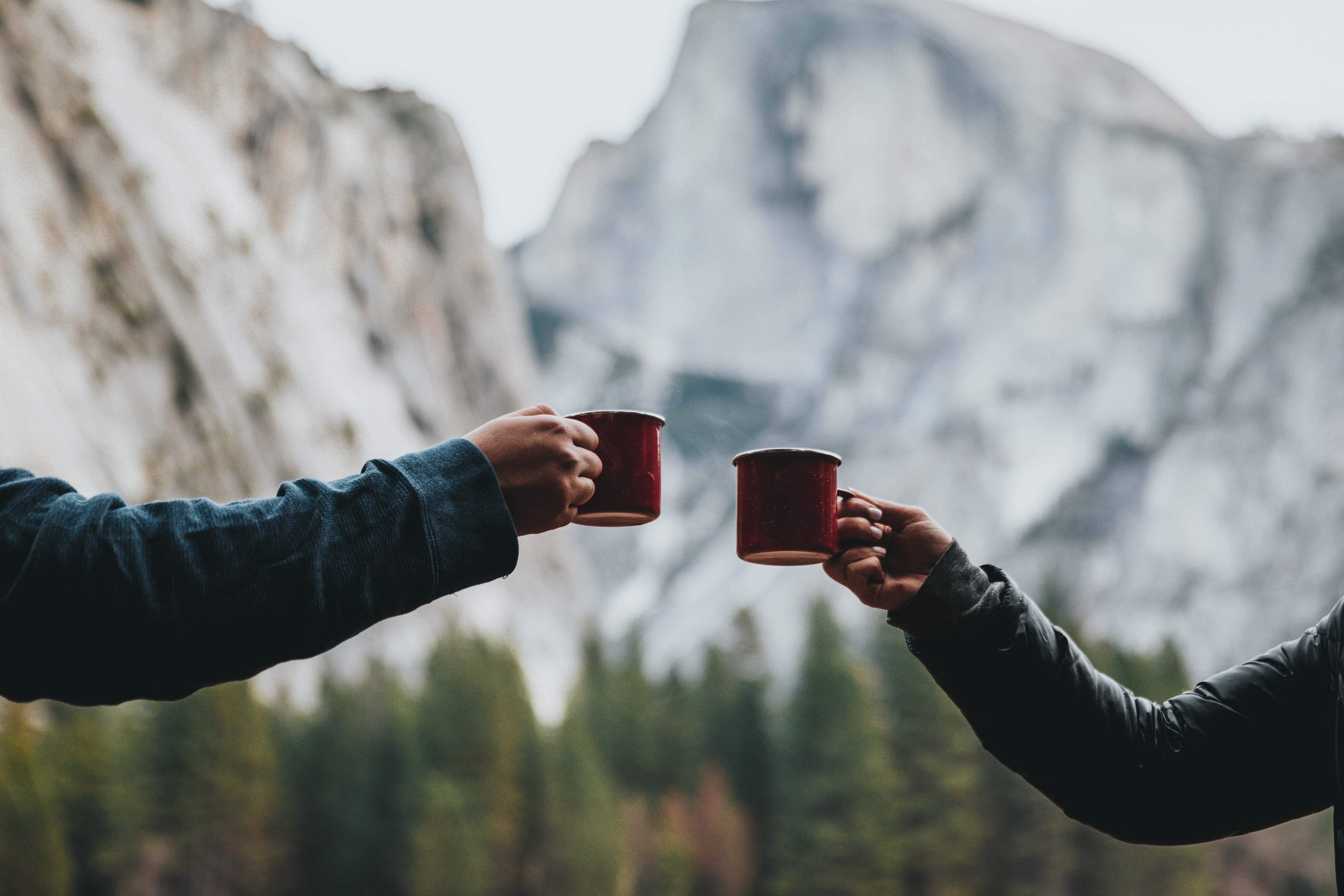 Two hands holding mugs on a hike stopping for food