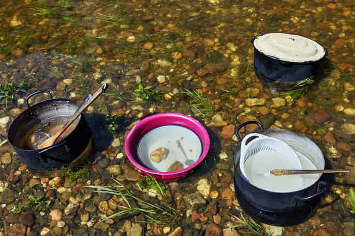 dirty camping cookware in a river in the middle of the cleaning process
