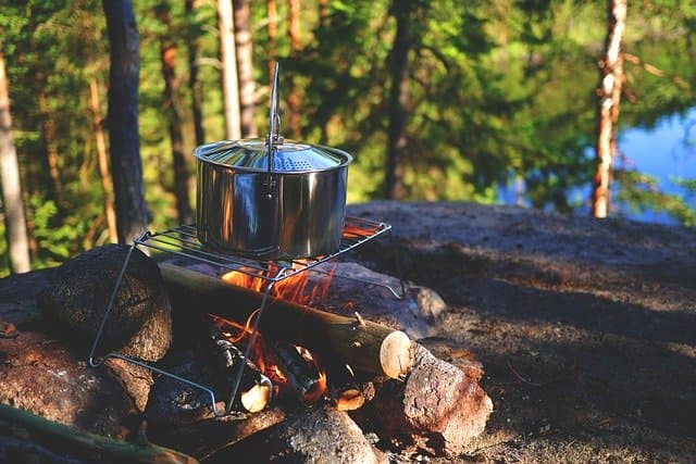 a metal pot over a campfire in the middle of a campsite