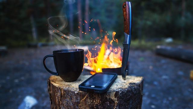 camping knife, mug, and phone on a log over a campfire