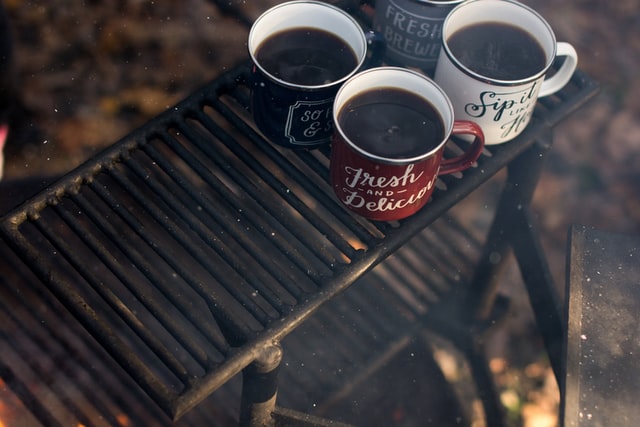 four cups of hot coffee heating over a campfire