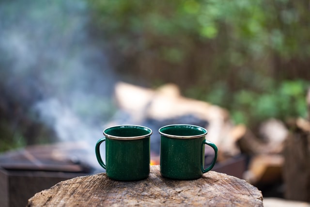 two green mugs of hot coffee overlooking a campsite