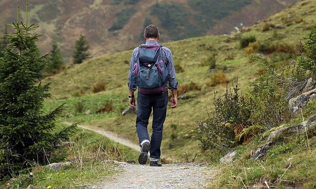 mountaineering man hiking down a path with his tent packed into his backpack
